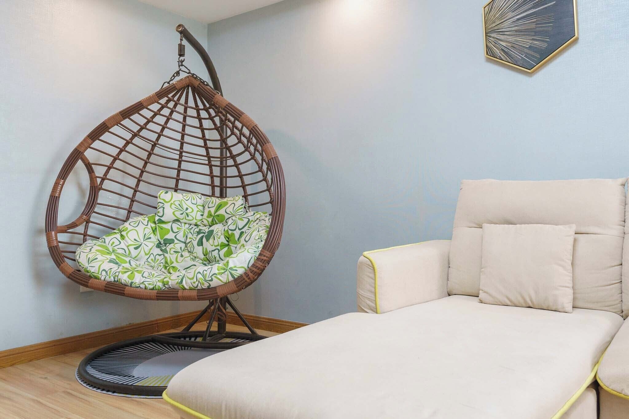 A room with a hanging chair, a sofa, and a framed artwork on the wall.