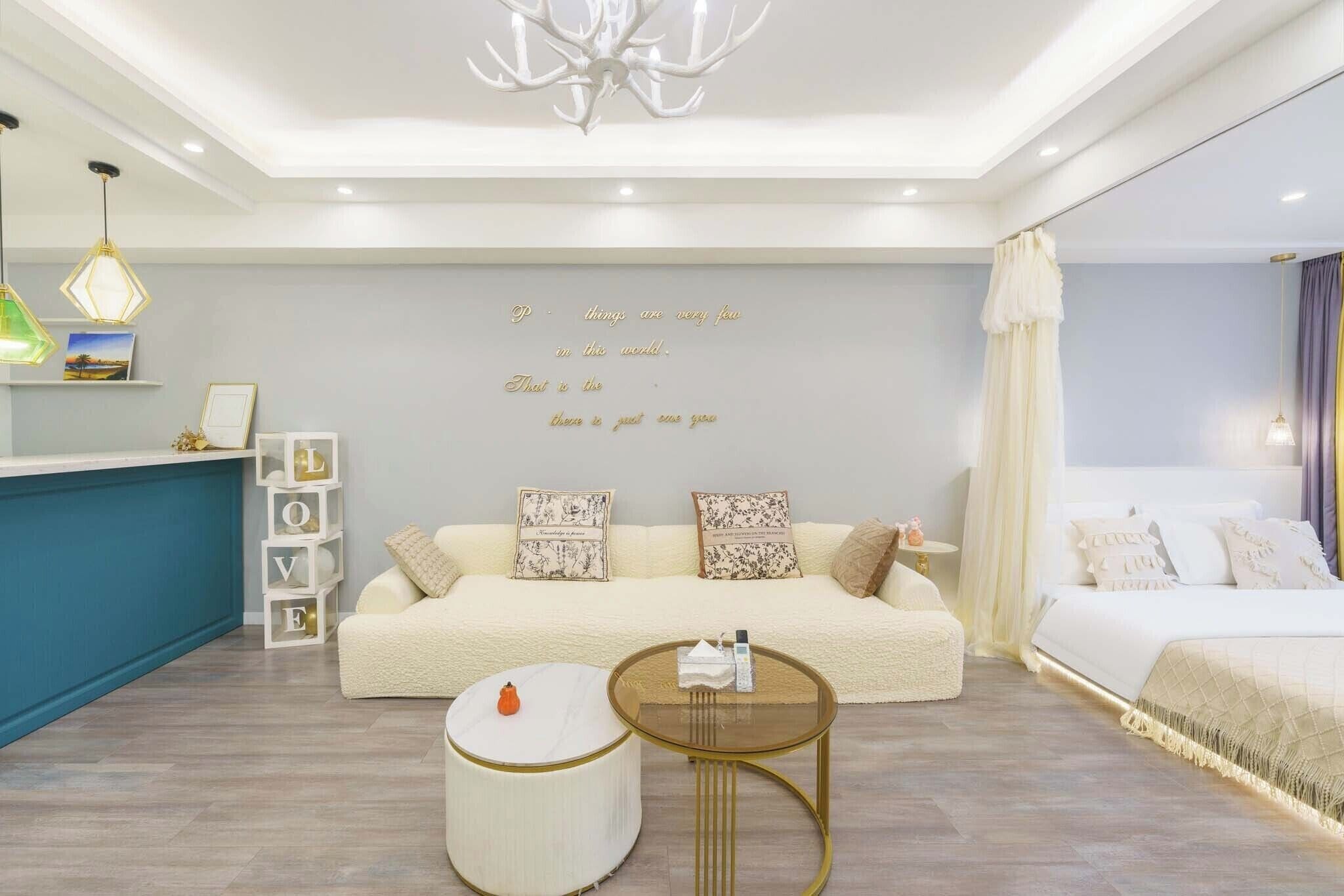 A modern bedroom with a bed, a sofa, a round coffee table, and a decorative wall with a quote.