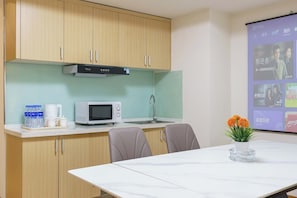 A kitchen with wooden cabinets, a microwave, and a sink. There is a table with chairs and a projector screen displaying images. - Qingni No. 8 Hotel Apartment (Dalian)