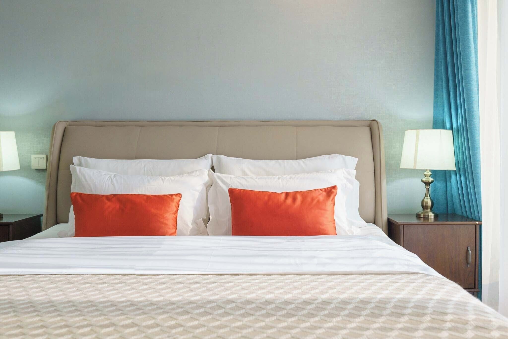 A hotel room with a bed, two pillows, a nightstand, a lamp, and a curtain.