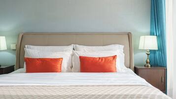 A hotel room with a bed, two pillows, a nightstand, a lamp, and a curtain.