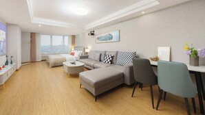 A modern living room with a sofa, ottoman, and chairs, a dining area with a table, and a large window with a view. - Qingni No. 8 Hotel Apartment (Dalian)