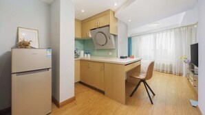 A compact kitchen with a built-in oven, a small dining area with a chair, and a TV. - Qingni No. 8 Hotel Apartment (Dalian)