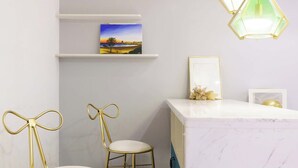 A room with a white marble counter, two gold chairs with bow designs, a framed picture on a shelf, and a green pendant light. - Qingni No. 8 Hotel Apartment (Dalian)