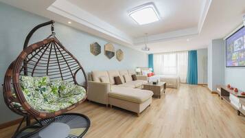 Una sala de estar con un sillón colgante, un juego de sofá, una mesa de centro y una pantalla de televisión.