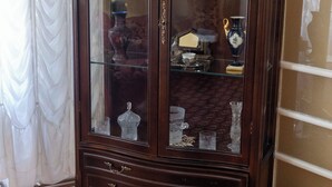 Un mueble de madera oscura con puertas de cristal, una lámpara verde en su interior y varios objetos decorativos en las repisas.