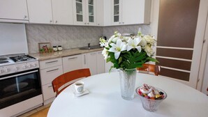 Una cocina con armarios blancos, una estufa, horno y una mesa de comedor con un florero y un cuenco de aperitivos.