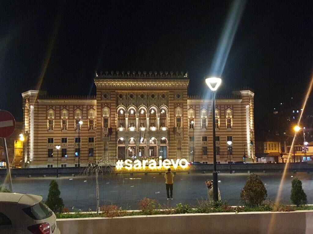 Un grand bâtiment illuminé, doté d’une entrée imposante et d’une enseigne sur laquelle on peut lire « Sarajevo ».