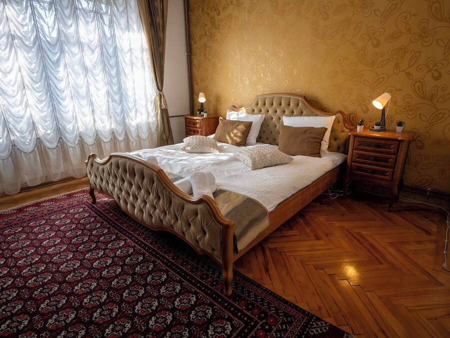 Ein Schlafzimmer mit einem großen Bett, Holzboden, einem gemusterten Teppich und einem Nachttisch mit Lampe.
