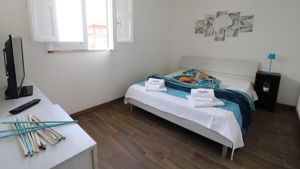 Un dormitorio con cama, un escritorio con computadora y palillos, televisor y obras de arte en la pared.