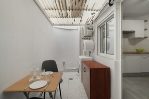 Cocina compacta con zona de comedor, paredes blancas, una mesa de madera y una ventana.