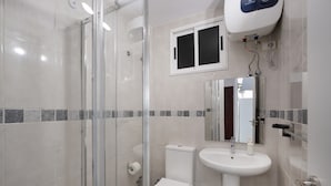 Kylpyhuoneessa on lasiseinällinen suihkukaappi, wc-istuin, pesuallas ja ikkuna wc-istuimen yläpuolella.