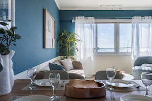 Un comedor con una mesa preparada para cuatro personas, un sofá, una planta y vista al mar.