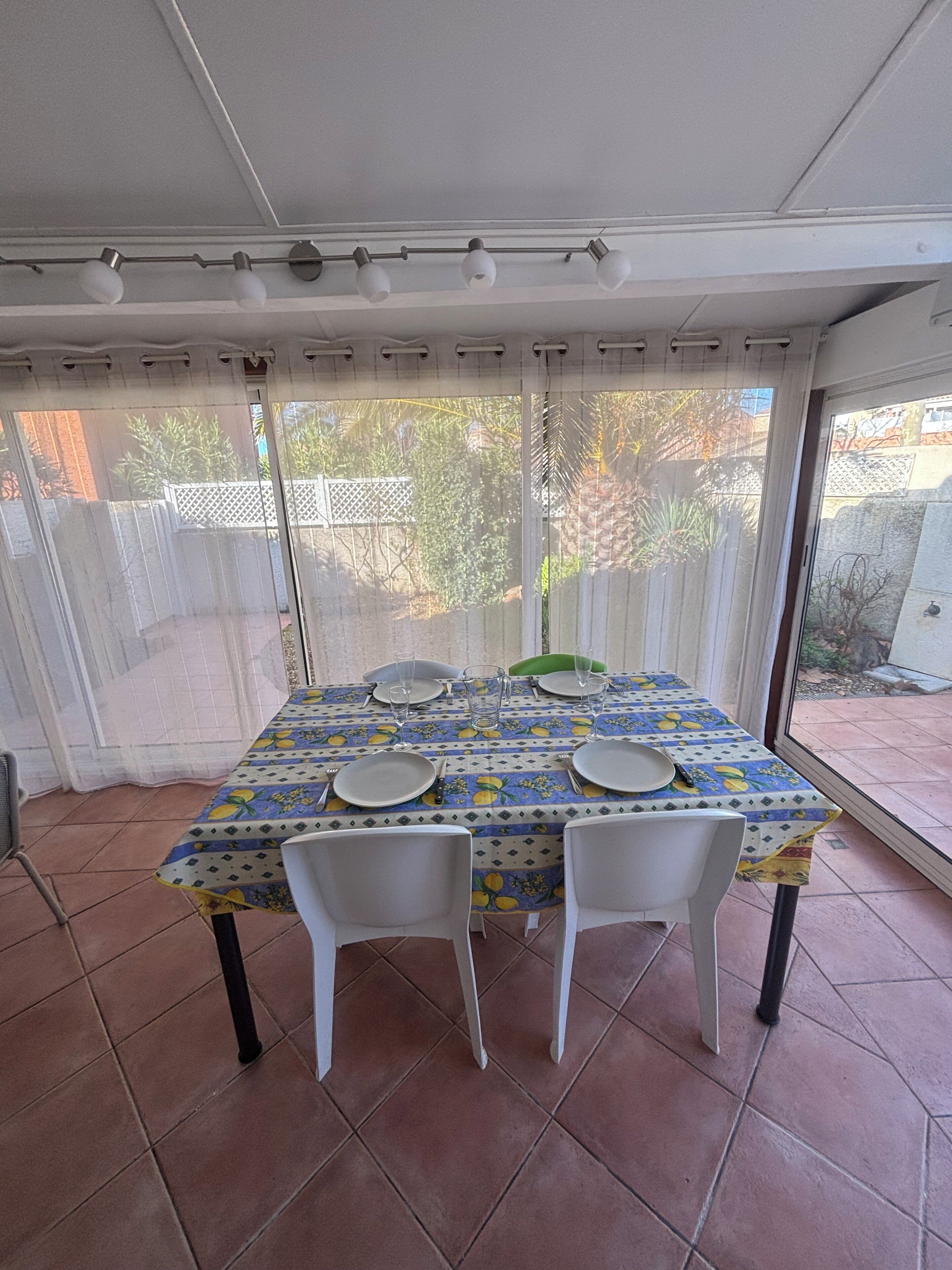 Un patio techado con una mesa para dos, sillas y vistas al jardín trasero.