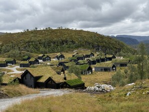 Un conjunto de edificios negros con techos de hierba, rodeados por un paisaje natural con colinas y árboles.
