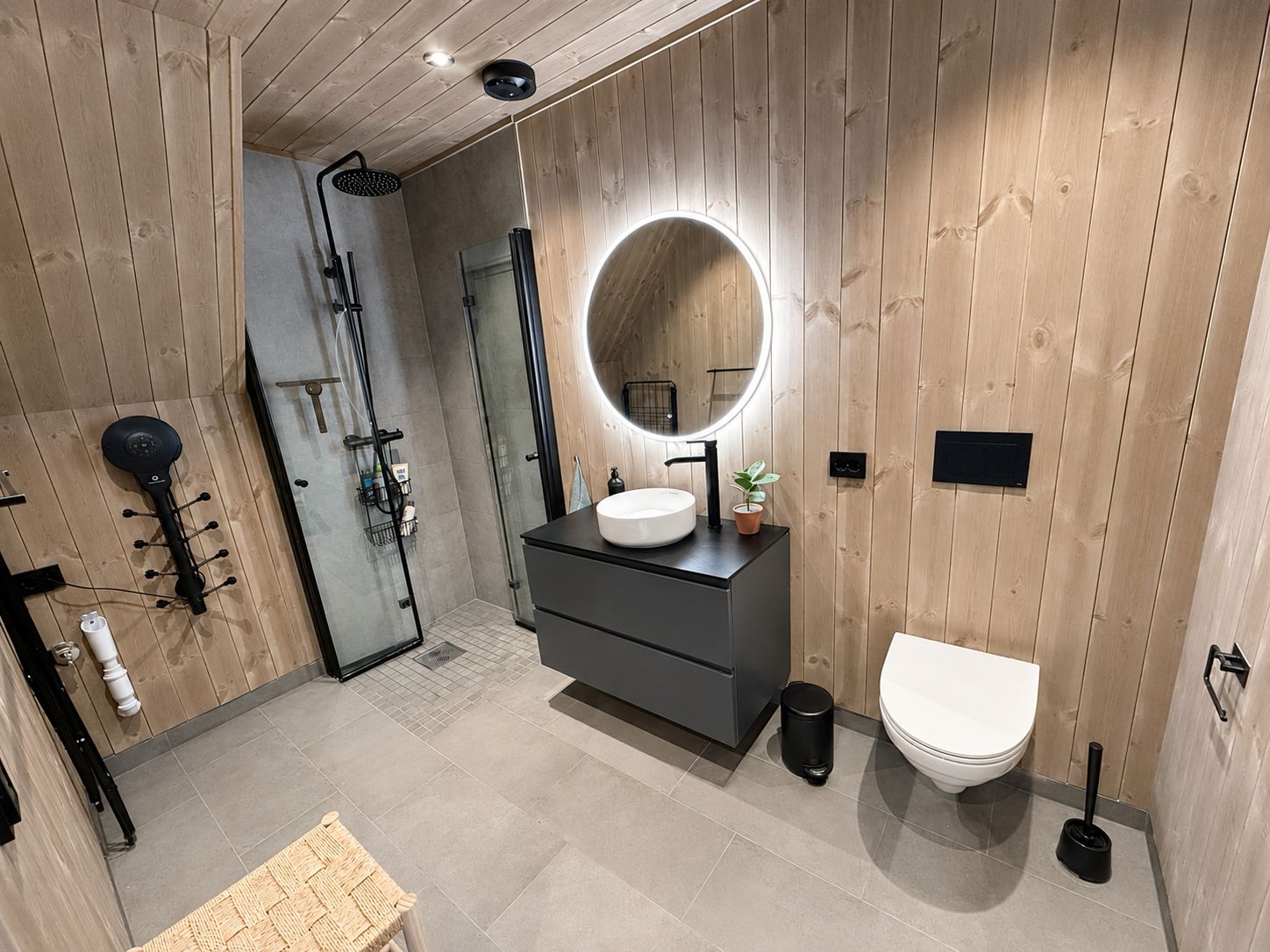 Une salle de bain moderne avec un mur en bois, un miroir rond, un lavabo et des toilettes.