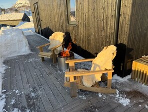 A wooden cabin with a fireplace, a bench, and a snow-covered deck.