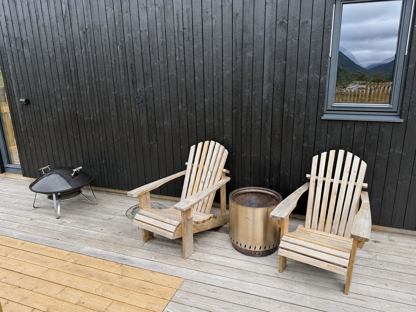 A wooden deck with two Adirondack chairs and a grill.
