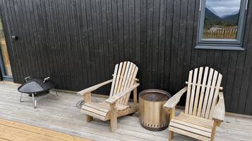 A wooden deck with two Adirondack chairs and a grill.
