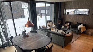 Una sala de estar moderna con una mesa de comedor, sofás, una chimenea y ventanas amplias.