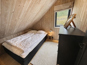 A small, sloped-roofed room with a bed, a desk, and a window.