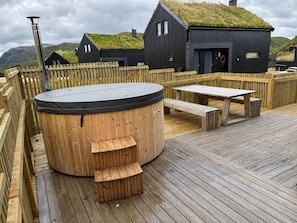 A wooden deck with a hot tub, picnic table, and benches.