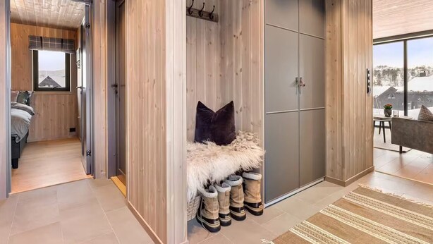 A modern interior with a wooden floor, a fur-covered bench, boots, and a large wardrobe.
