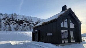A wooden building with large windows and a sloped roof, surrounded by snow-covered landscape.