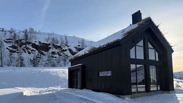 A wooden building with large windows and a sloped roof, surrounded by snow-covered landscape.
