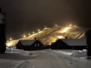 A snow-covered landscape with buildings and a lit ski slope.