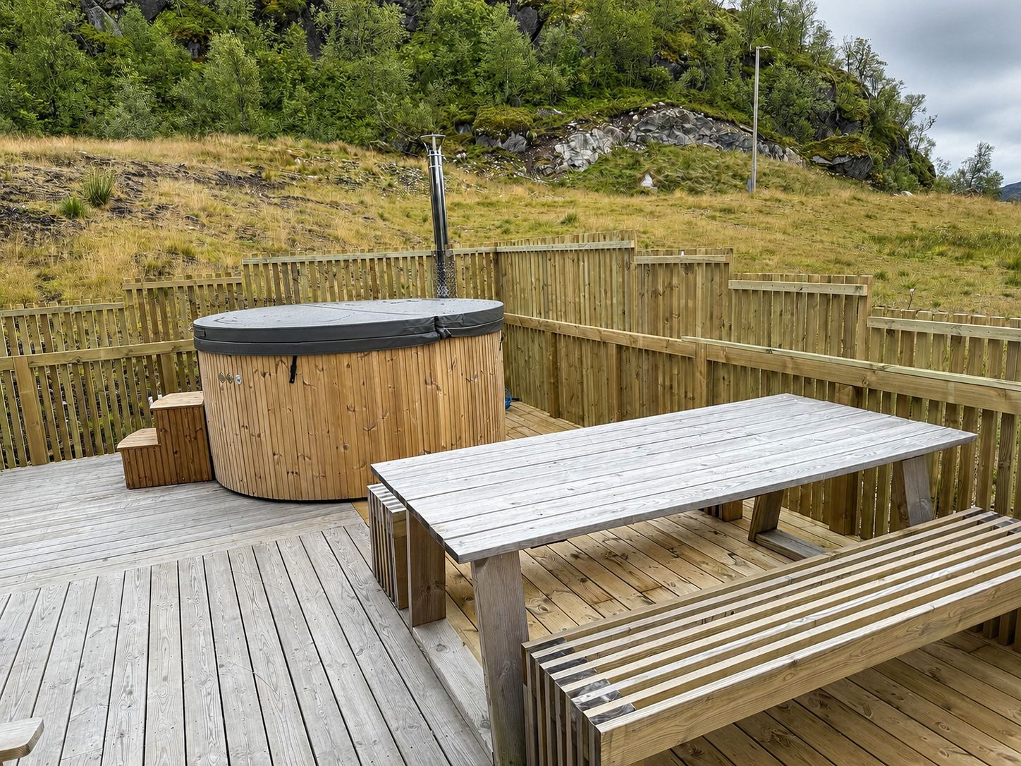 Una terraza de madera con un jacuzzi, una mesa y bancos.