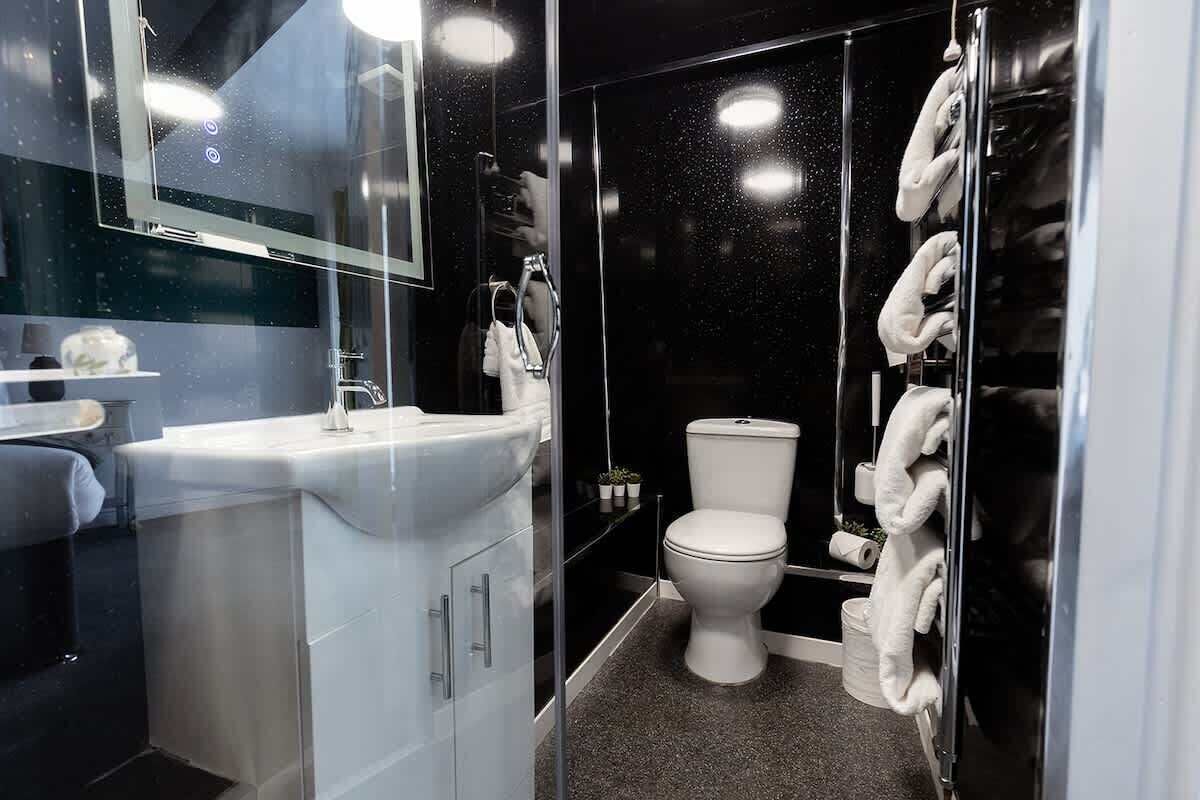 Un baño moderno con cabina de ducha de vidrio, inodoro blanco y lavamanos con espejo superior.