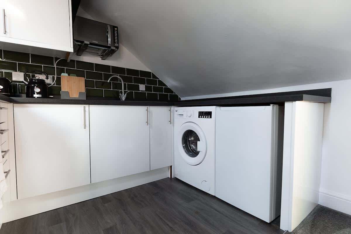 A compact kitchen with white cabinets, a built-in washing machine, and a microwave.