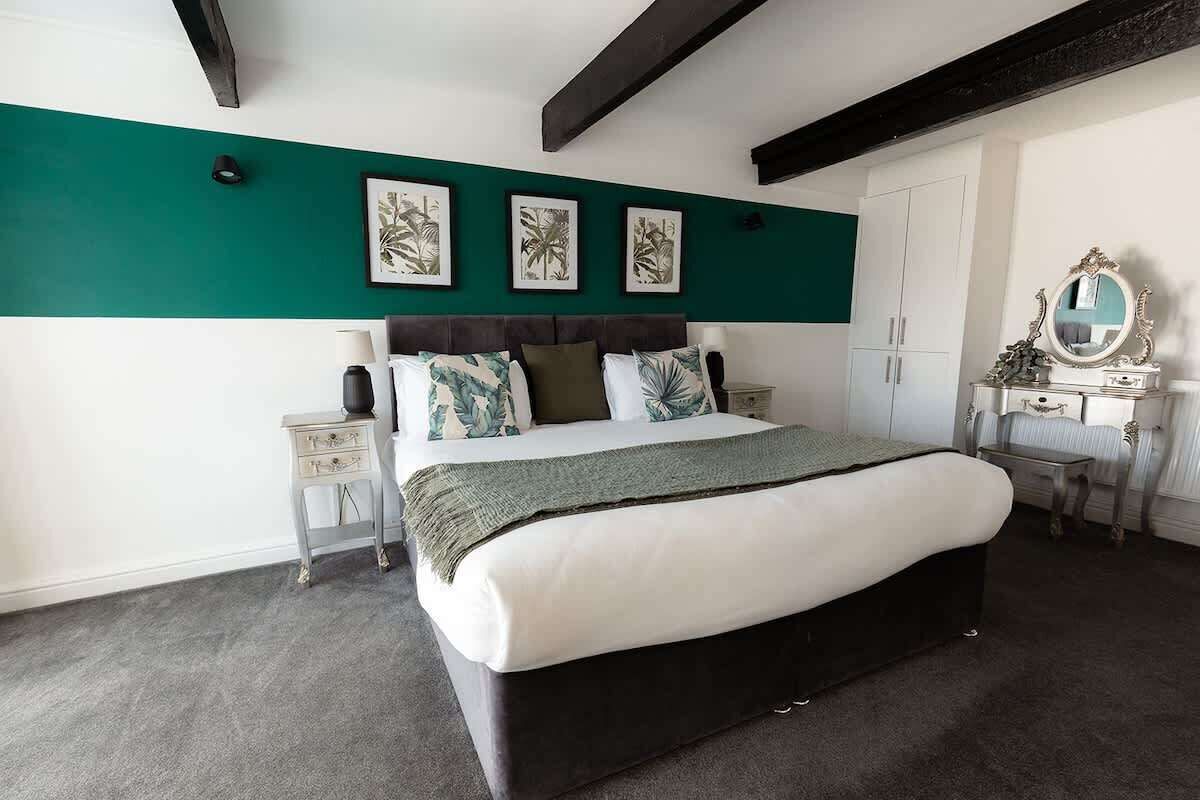 Une chambre à coucher comprenant un lit, une table de chevet, une commode, un miroir et des œuvres d’art encadrées accrochées au mur.