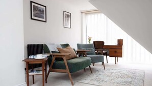 A modern living room with a green sofa, a blue armchair, a wooden side table, and a small wooden cabinet.