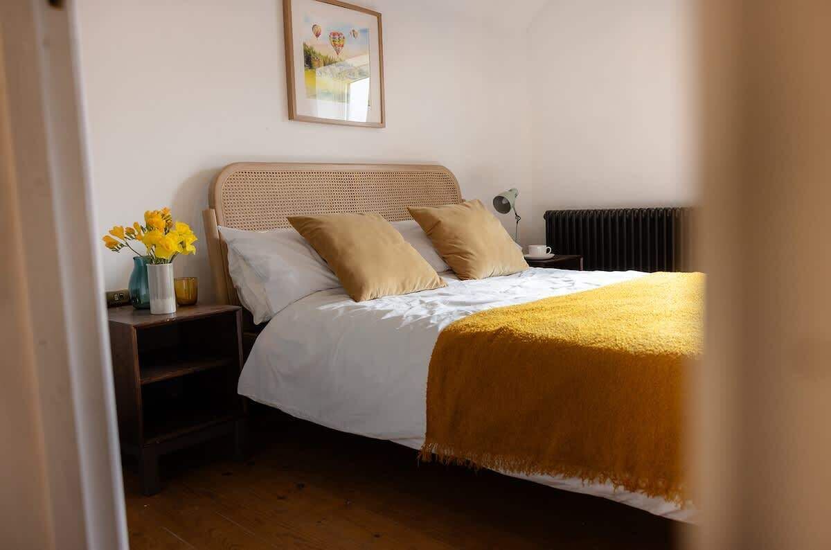 A bedroom with a bed, bedside table, lamp, and a framed picture on the wall.