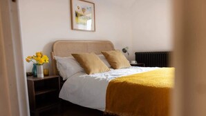 A bedroom with a bed, bedside table, lamp, and a framed picture on the wall.