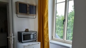 Una habitación pequeña con una mesa, un microondas, un armario, una silla y una ventana con cortinas.