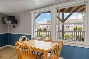 A dining area with a table and chairs, a flat-screen TV mounted on the wall, and large windows with a view of the outside. - Ocean Air Suites 300 Feet from Beach, Strip (Hampton)