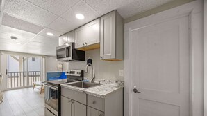 A modern kitchen with stainless steel appliances, a granite countertop, and a sliding glass door leading to a balcony. - Ocean Air Suites 300 Feet from Beach, Strip (Hampton)