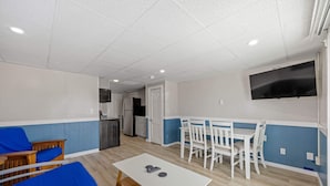 A room with a white table, blue sofa, white chairs, a TV, and a kitchenette. - Ocean Air Suites 300 Feet from Beach, Strip (Hampton)