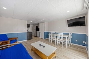 A room with a white table, blue sofa, white chairs, a TV, and a kitchenette. - Ocean Air Suites 300 Feet from Beach, Strip (Hampton)