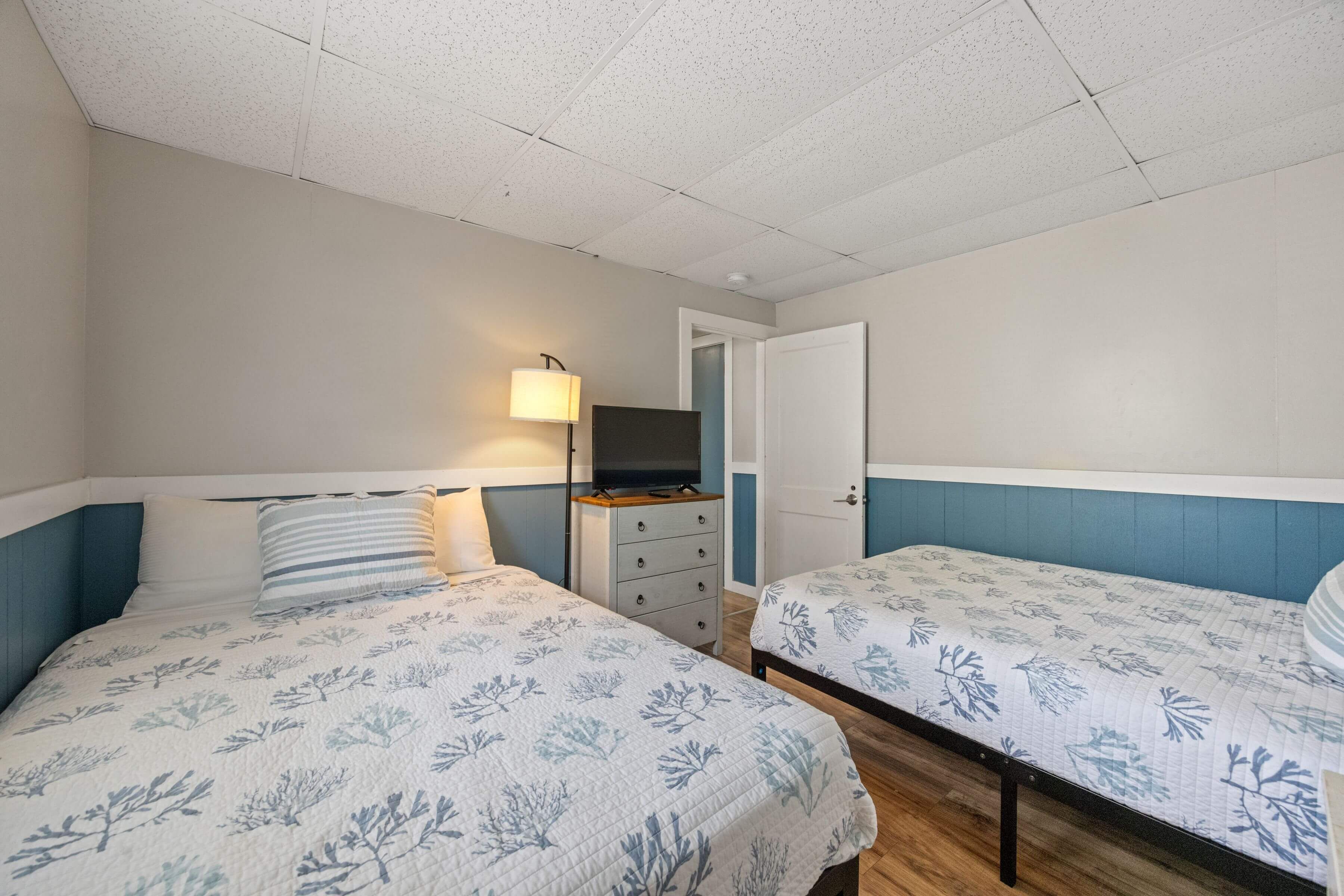 A bedroom with two beds, a dresser, a television, and a door.