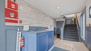 A reception desk with a 'WELCOME' sign, a fire extinguisher, and a staircase leading to the upper floor. - Ocean Air Suites 300 Feet from Beach, Strip (Hampton)