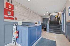 A reception desk with a 'WELCOME' sign, a fire extinguisher, and a staircase leading to the upper floor. - Ocean Air Suites 300 Feet from Beach, Strip (Hampton)