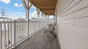 A wooden deck with white railings, a covered area, and a view of buildings in the background. - Ocean Air Suites 300 Feet from Beach, Strip (Hampton)