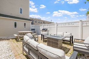 Eine Terrasse mit Gartenmöbeln, einem Grill und einem weißen Zaun.