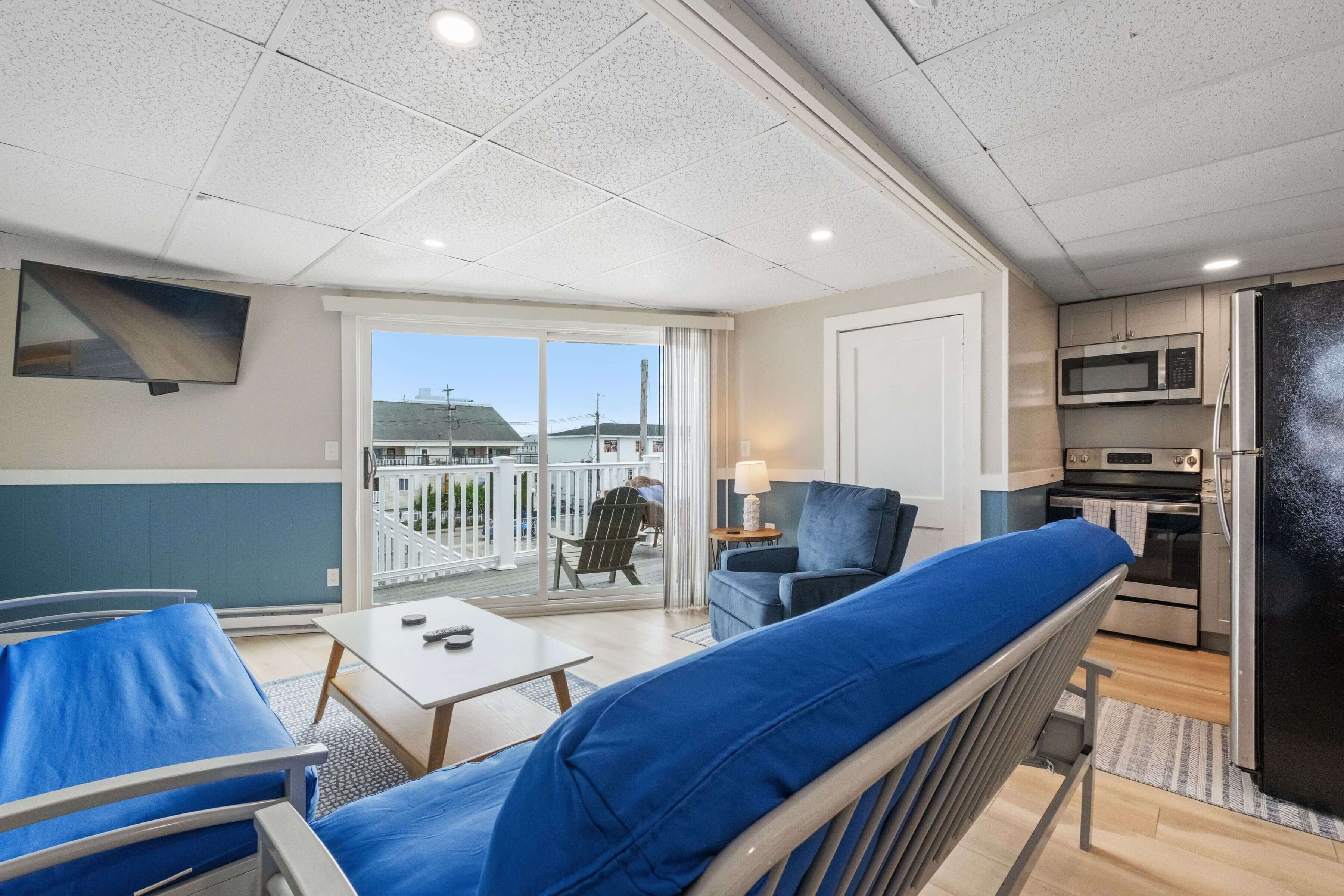 A modern room with a balcony, a sofa, a table, a TV, and a kitchen area.