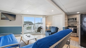 A modern room with a balcony, a sofa, a table, a TV, and a kitchen area. - Ocean Air Suites 300 Feet from Beach, Strip (Hampton)