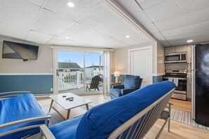 A modern room with a balcony, a sofa, a table, a TV, and a kitchen area. - Ocean Air Suites 300 Feet from Beach, Strip (Hampton)